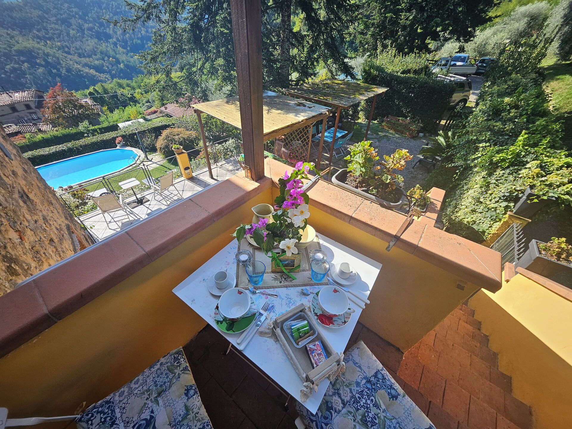 A balcony with a table set for a meal, overlooking a swimming pool and lush greenery.