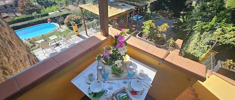 A balcony with a table set for a meal, overlooking a swimming pool and lush greenery.