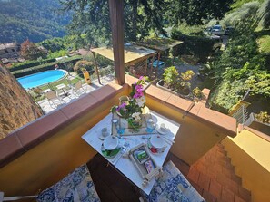 Un balcon avec une table dressée pour un repas, donnant sur une piscine et une végétation luxuriante.