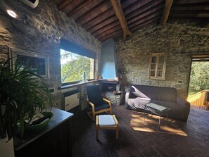 Un intérieur rustique avec des murs en pierre, un plafond en bois, une cheminée en pierre, un canapé, un fauteuil et une table.