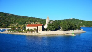 Une église côtière dotée d’un clocher, entourée d’un mur de pierre et de palmiers, qui surplombe une mer calme.