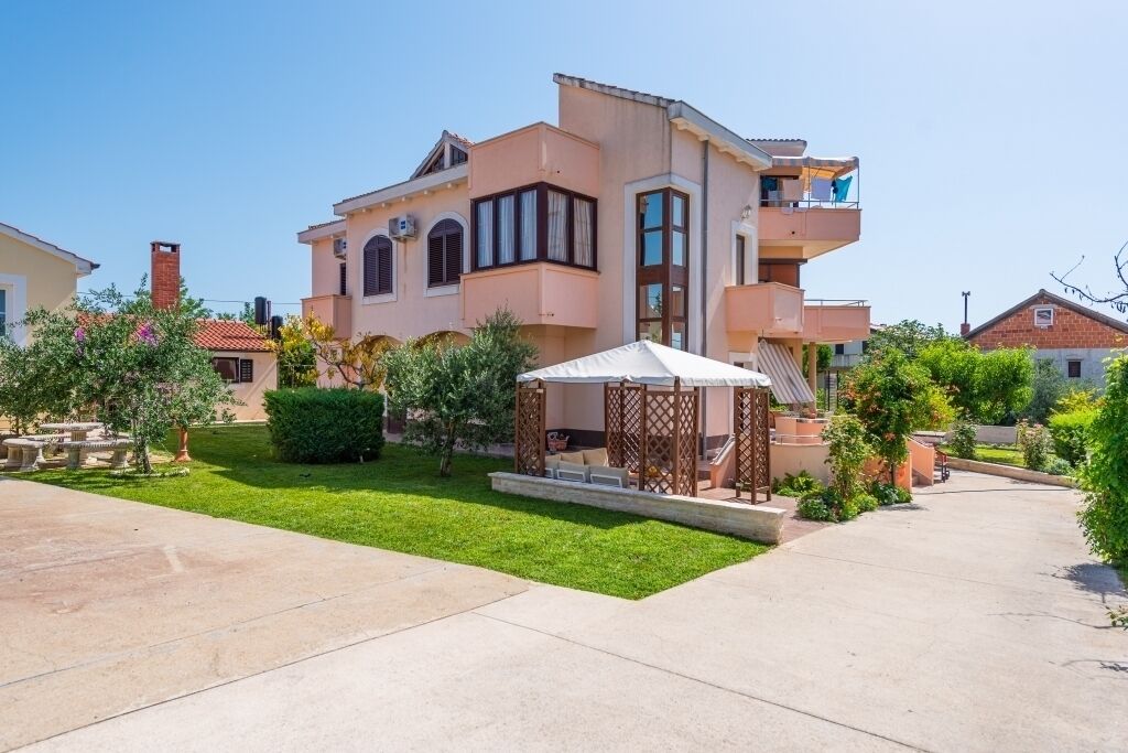A two-story house with a balcony, a covered outdoor seating area, and a well-maintained lawn.
