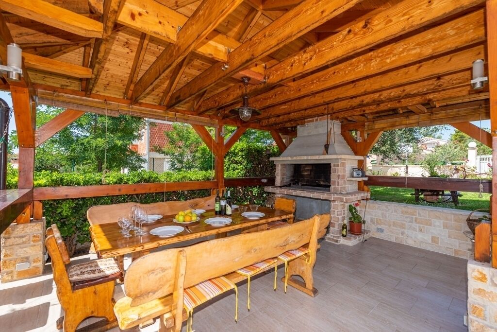 An outdoor wooden pergola with a built-in grill and seating area.