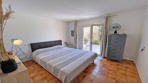 Une chambre à coucher comprenant un lit, une table de chevet, une lampe, une commode et une vue sur l’extérieur.