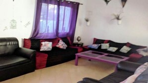 A living room with a black sofa, a purple coffee table, and a black sofa with red and blue cushions.
