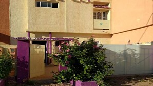 A two-story building with a purple entrance and a small garden with pink flowers.
