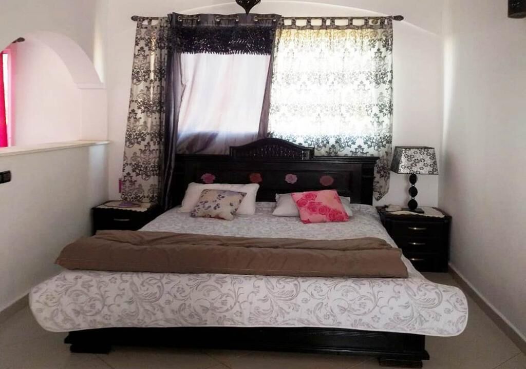 Une chambre à coucher avec un lit, une table de chevet, une lampe et une fenêtre avec des rideaux.
