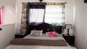 A bedroom with a bed, a nightstand, a lamp, and a window with curtains.