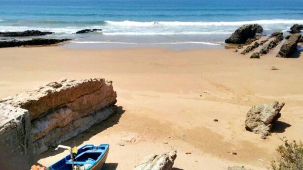 A beach with a boat, rocky formations, and the ocean.