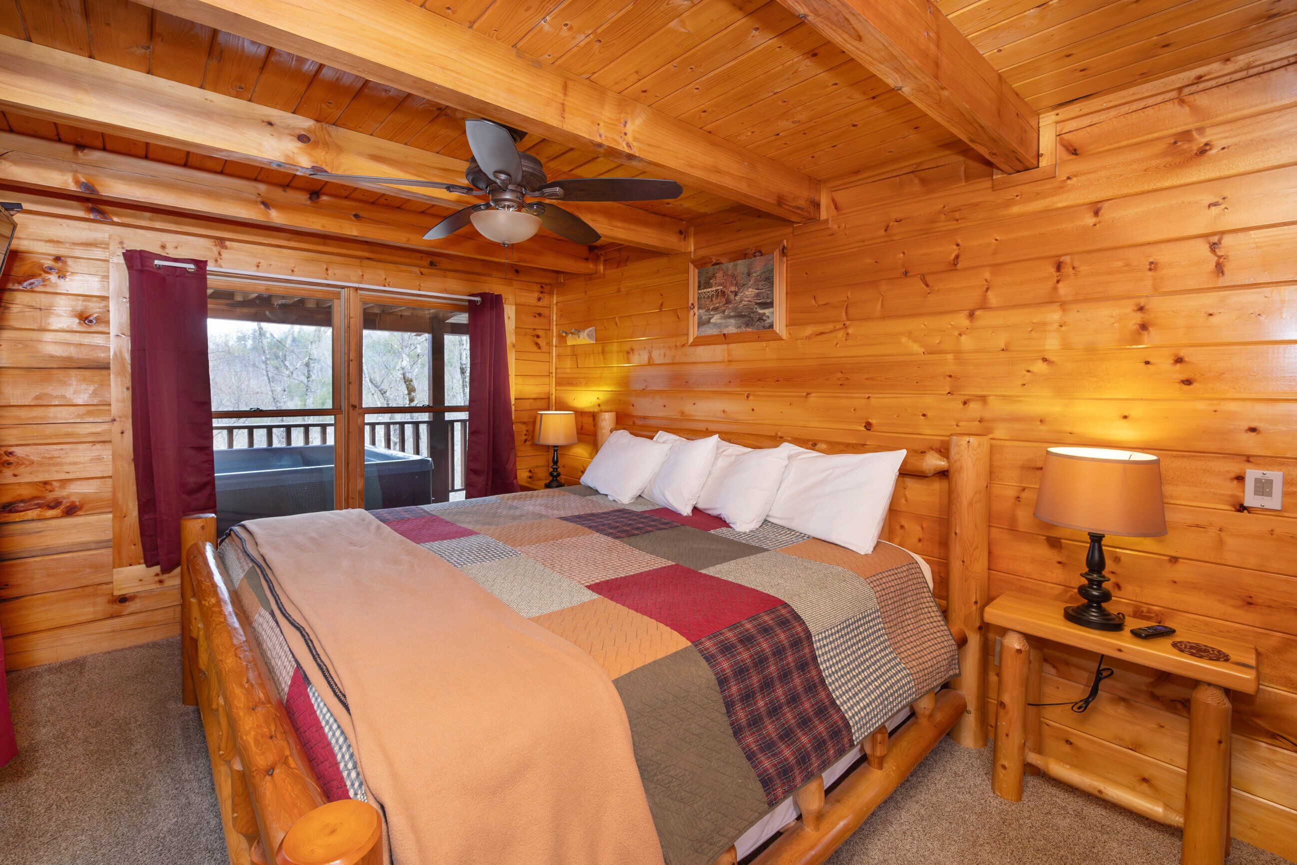 Ein Schlafzimmer einer Holzhütte mit einem Bett, einem Deckenventilator, einem Nachttisch mit Lampe und einem Fenster mit Vorhängen.