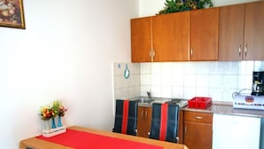 Una cocina compacta con armarios de madera, una mesa de comedor con un camino de mesa rojo y un refrigerador pequeño.