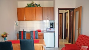 Un espacio habitable compacto con área de cocina, una mesa de comedor con sillas y un sofá rojo.