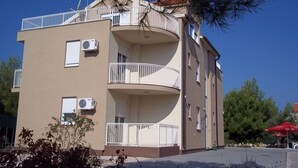 A multi-story building with balconies, air conditioning units, and a red umbrella in the foreground. - Apartment in Vodice with Terrace, Air condition, WIFI (3599-8) (Vodice)
