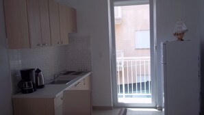 A compact kitchen with a sink, stove, and cabinets. There is a refrigerator and a small table with a grid-patterned placemat. A door leads to an outdoor balcony. - Apartment in Vodice with Terrace, Air condition, WIFI (3599-8) (Vodice)