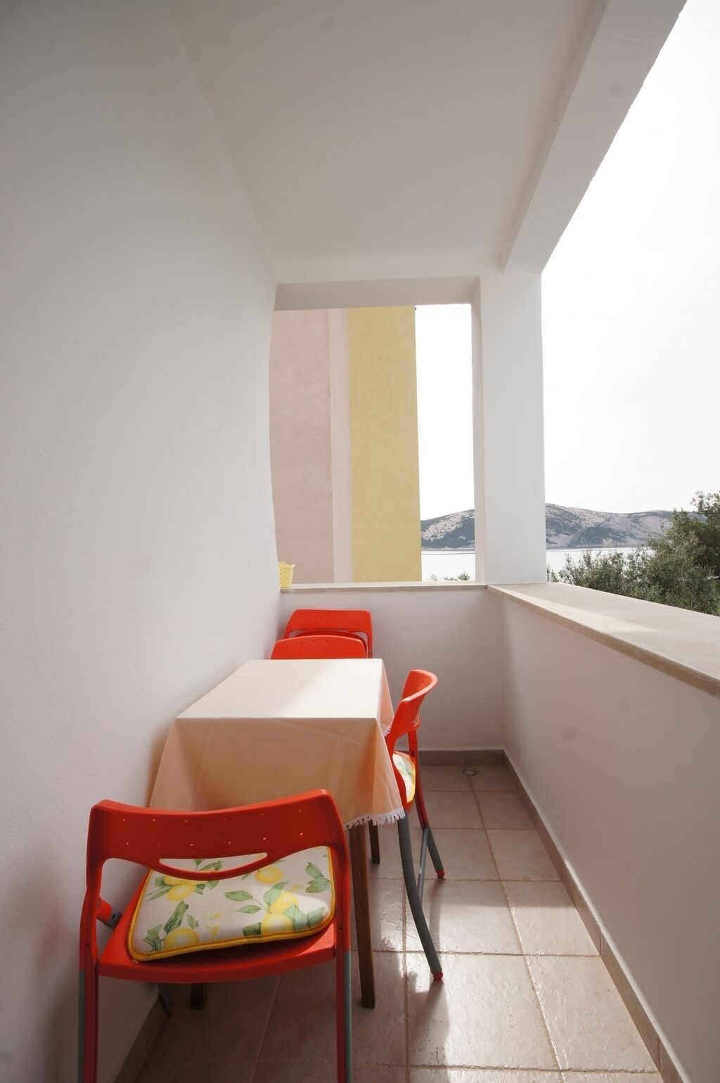 En balkon med bord og stole, havudsigt og et vindue med farverige gardiner.