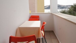 Un balcone con tavolo e sedie, vista sul mare e una finestra con una tenda colorata.