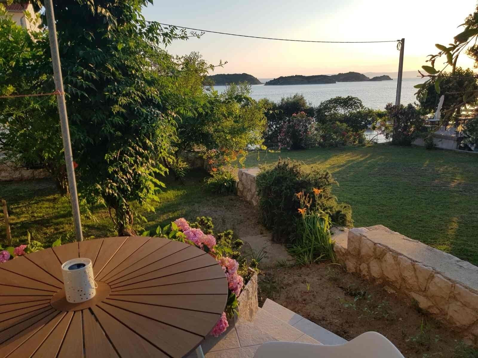 A patio with a wooden table and a white cup, overlooking a landscaped garden and a body of water.