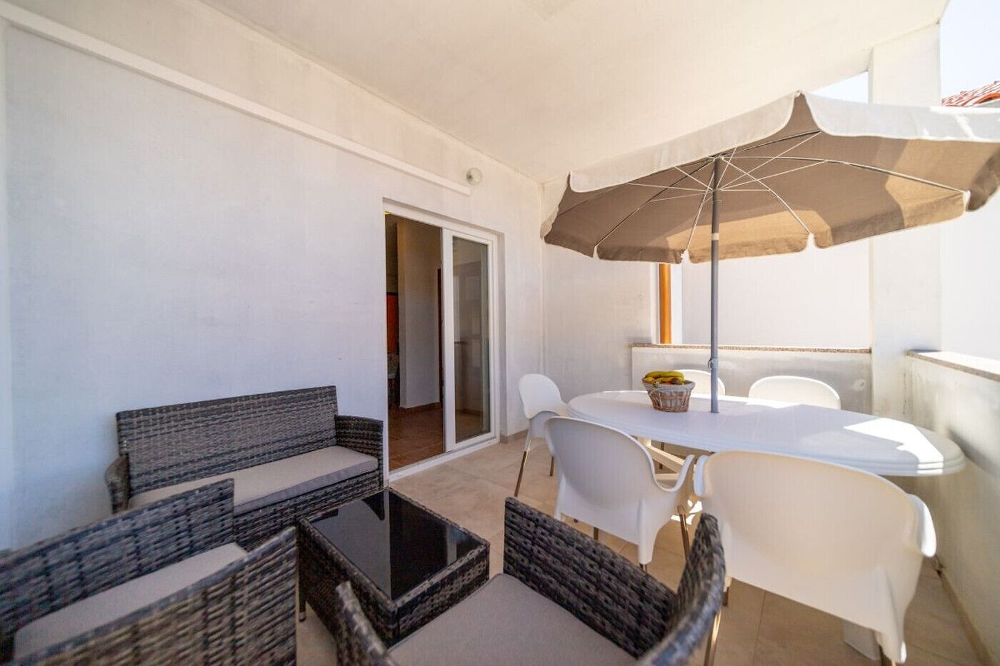 A balcony with a table and chairs, a wicker sofa, and a large umbrella.