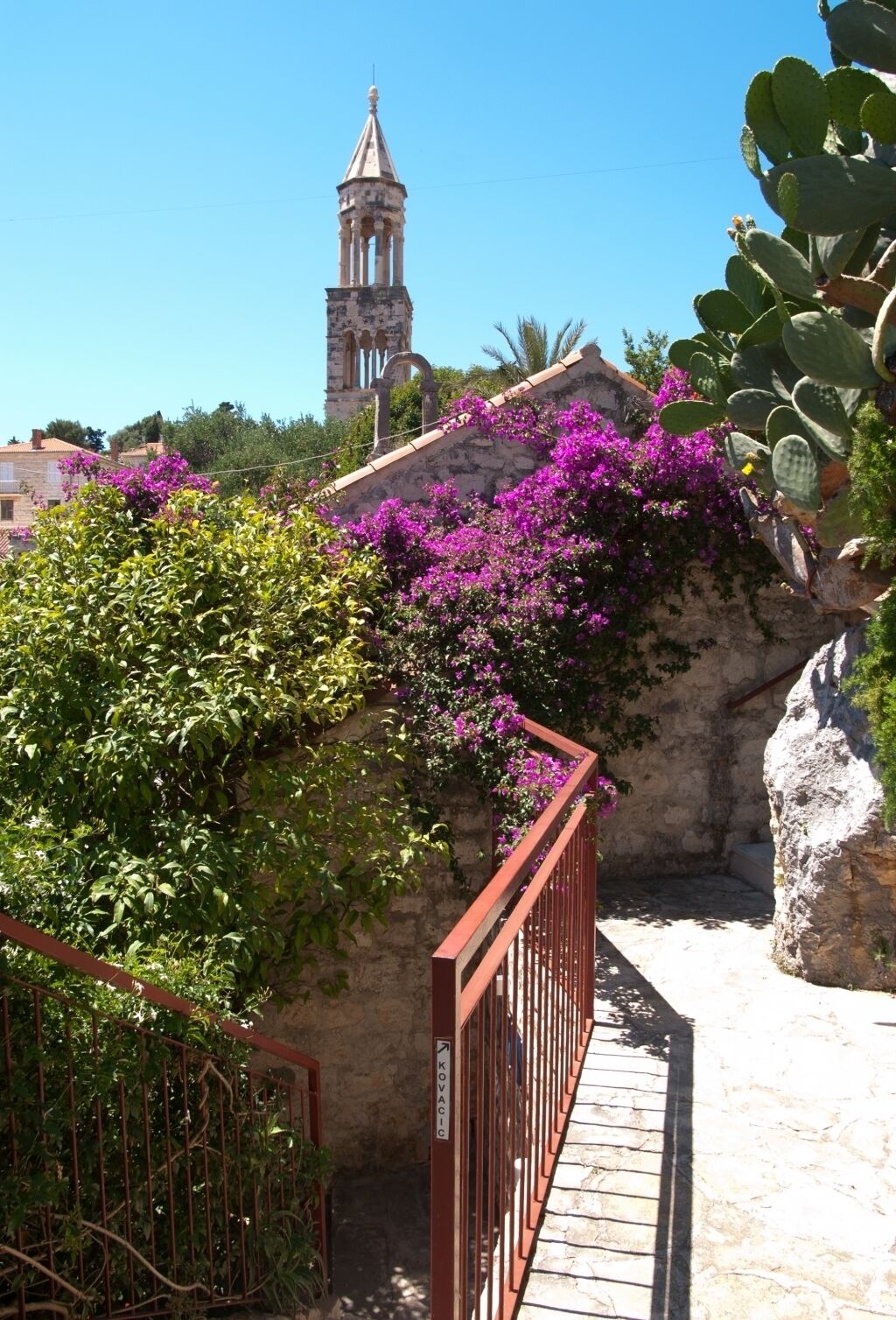 A stone staircase with a metal railing leading up to a building with a bell tower.