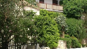 Ein weißes Gebäude mit Balkon, umgeben von üppiger Vegetation und einer Steinmauer.