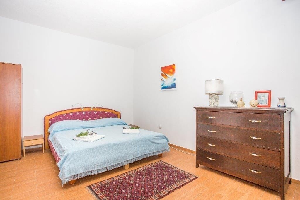 A bedroom with a bed, a dresser, a rug, and a painting on the wall.