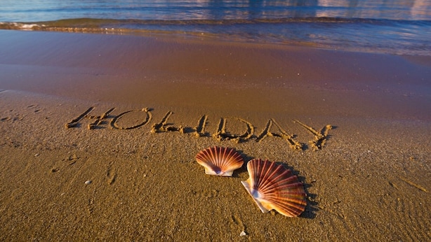 A beach with the word "HOLIDAY" written in the sand and two seashells.