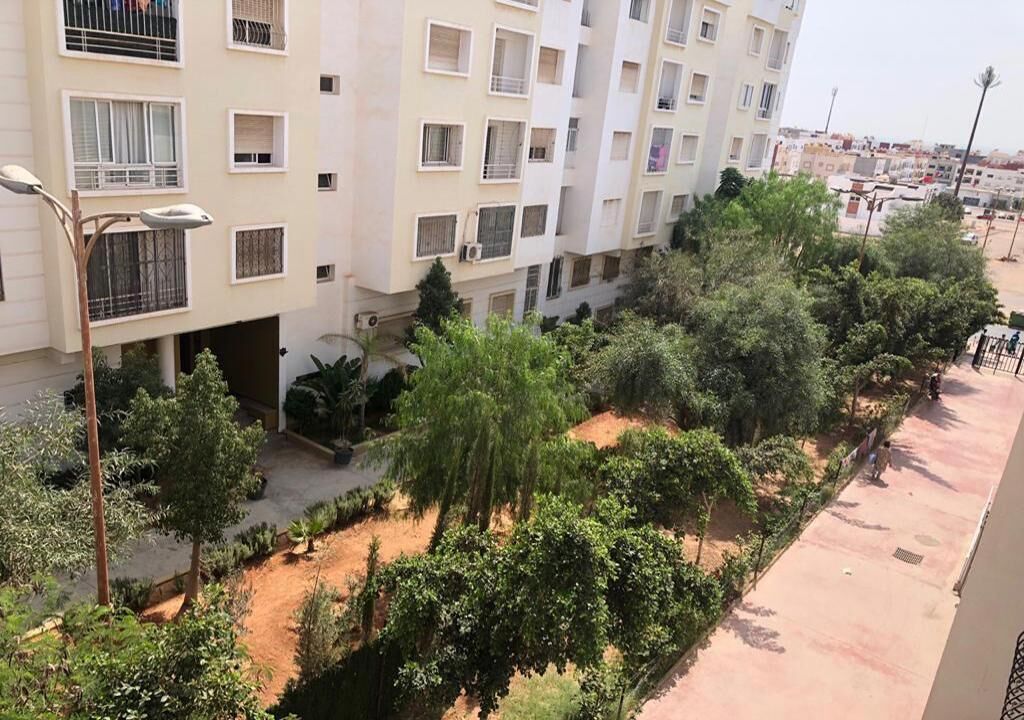 A multi-story residential building with balconies, a courtyard with trees, and a paved walkway.