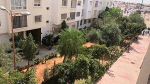 Ein mehrstöckiges Wohngebäude mit Balkonen, einem Innenhof mit Bäumen und einem gepflasterten Gehweg.