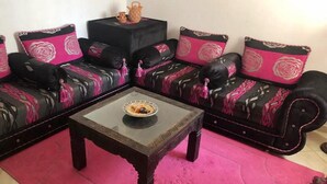 Ein Wohnzimmer mit einer schwarzen Couch, verziert mit floralen Kissen in Rosa und Weiß, einem kleinen schwarzen Beistelltisch und einem rosafarbenen Teppich.