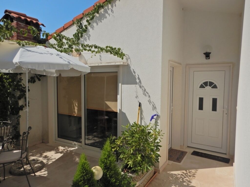 A covered patio with a table and chairs, a potted plant, and a door with a window.