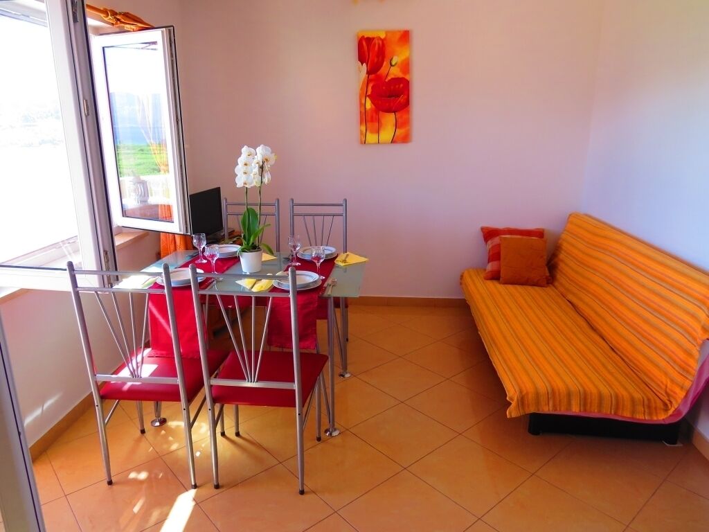 A dining area with a table set for two, a sofa, and a painting on the wall.