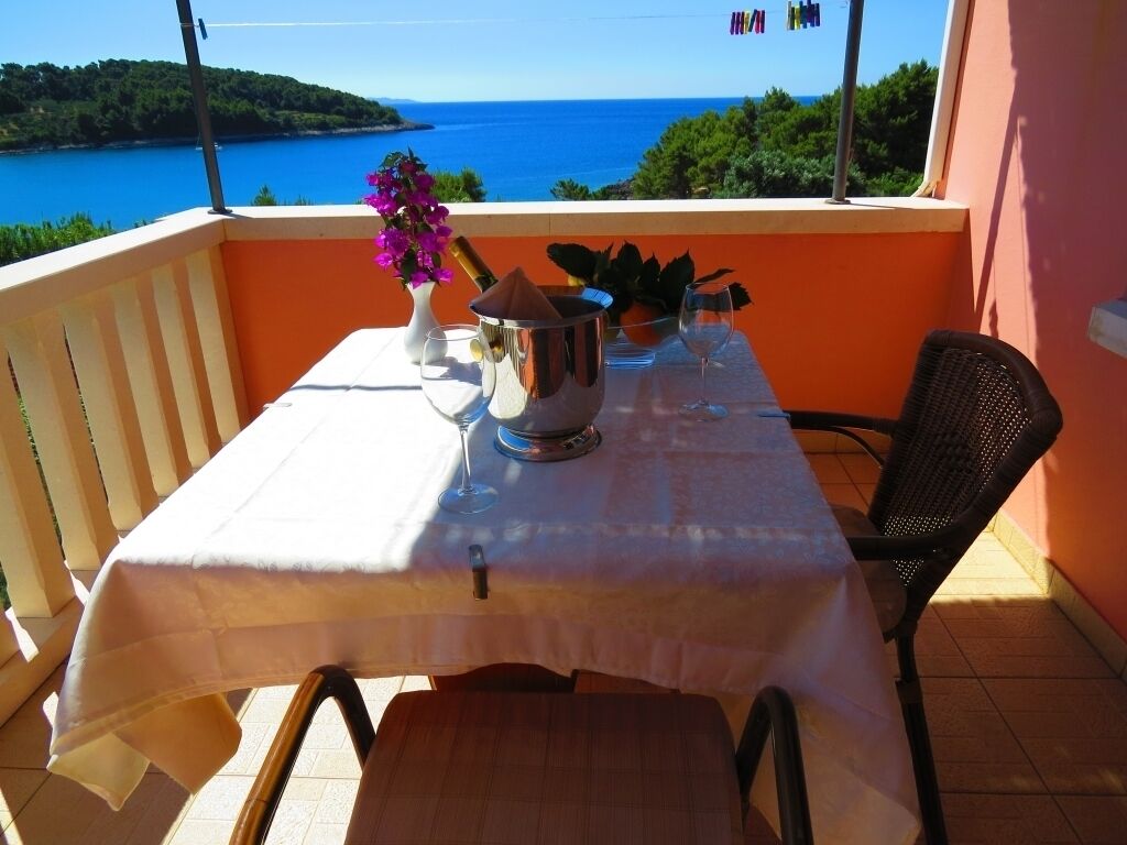 Een balkon met een tafel gedekt voor twee personen, een metalen bak, een vaas met bloemen en uitzicht op zee.