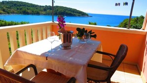 Un balcon avec une table dressée pour deux personnes, offrant une vue panoramique sur un plan d’eau et la verdure environnante.