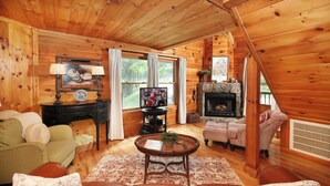 Interior acogedor de una cabaña de madera con chimenea, televisor y zona de estar confortable.