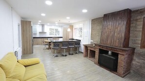 A modern living room with a yellow sofa, a fireplace, and a kitchen area in the background. - Villa Romera Rural Cottage for 25 people (Cardedeu)