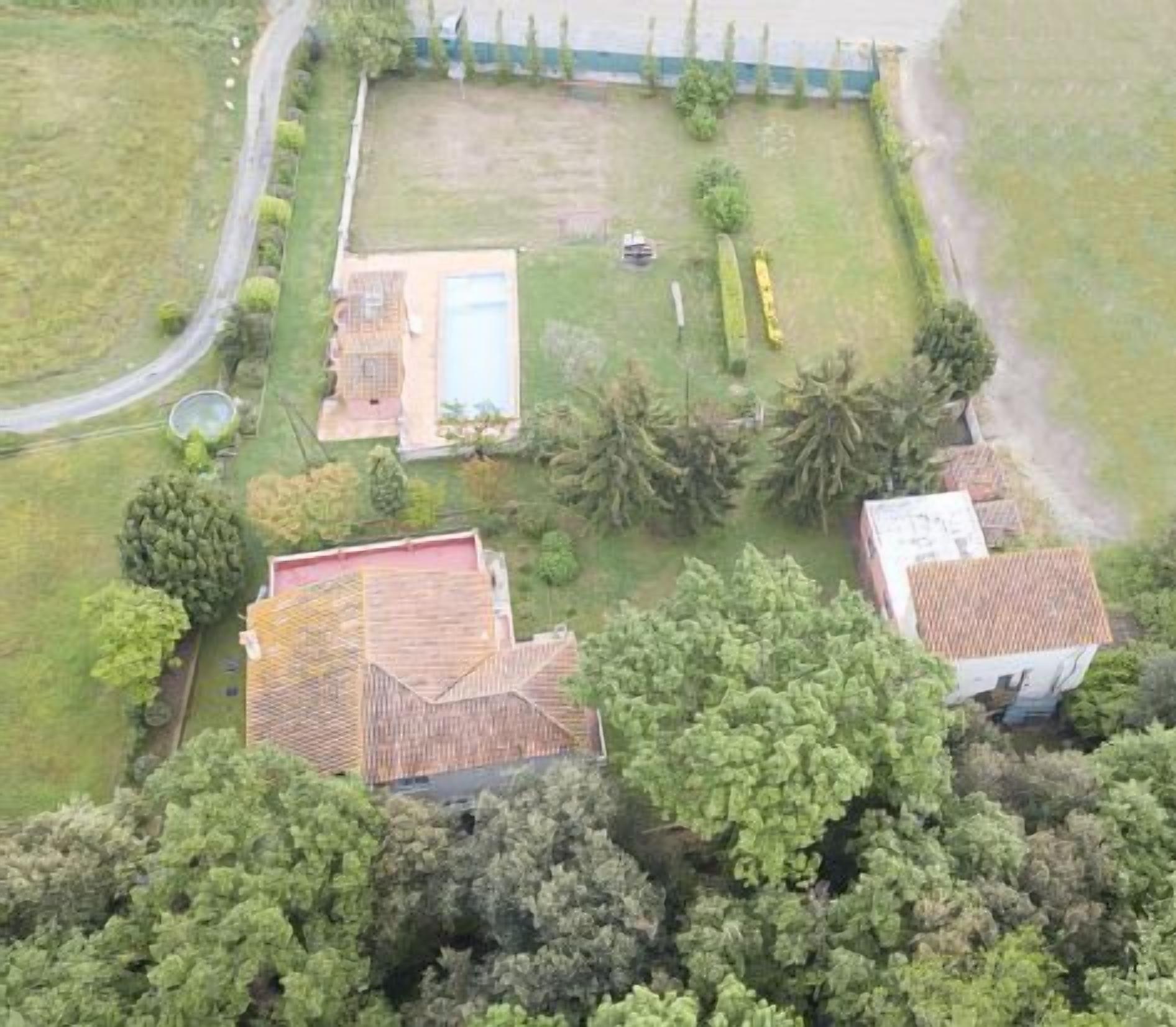 An aerial view of a residential area with two houses, one with a tiled roof and another with a red roof, surrounded by greenery and a small pool.