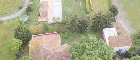 An aerial view of a residential area with two houses, one with a tiled roof and another with a red roof, surrounded by greenery and a small pool.