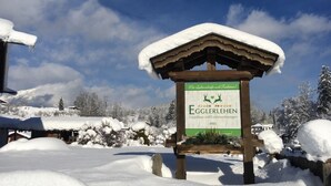A sign for Egglerlehen, a guesthouse and holiday homes, with a snowy landscape and mountains in the background. - Ferienwohnung  2 bis 2 Personen, 52 qm, Erdgeschoss, 1 separates Schlafzimmer, Terrasse (Schönau am Königssee)