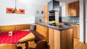 A kitchen with wooden cabinets, a central island, and a red tablecloth. - Ferienwohnung  2 bis 2 Personen, 52 qm, Erdgeschoss, 1 separates Schlafzimmer, Terrasse (Schönau am Königssee)