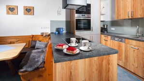 A compact kitchen with wooden cabinets, a built-in oven, and a dining area with a bench and table. - Ferienwohnung  2 bis 2 Personen, 52 qm, Erdgeschoss, 1 separates Schlafzimmer, Terrasse (Schönau am Königssee)
