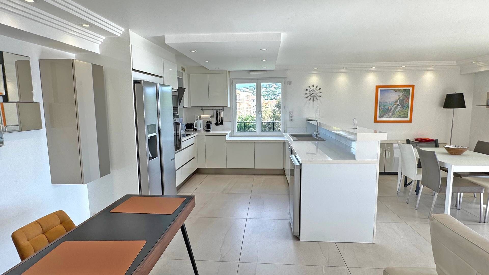 A modern kitchen with white cabinetry, a built-in island, and a dining area with a table and chairs.