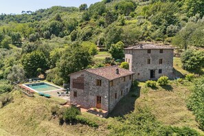 A stone building with a pool and a tower, surrounded by lush greenery.