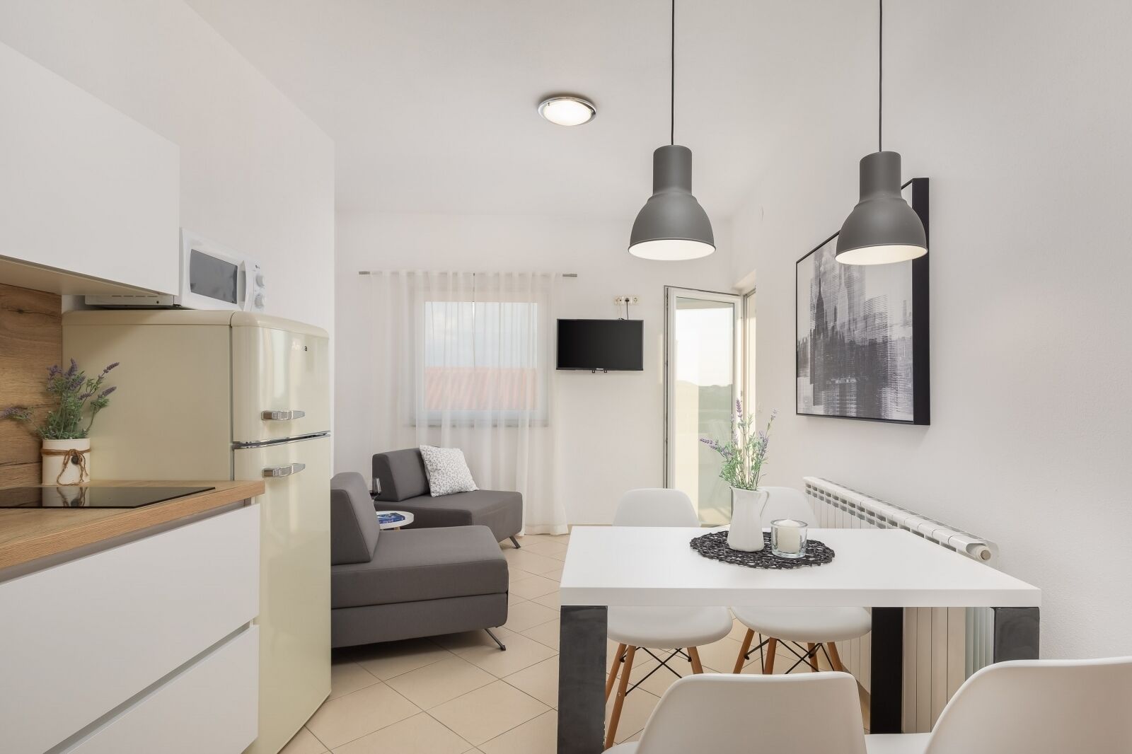 A modern kitchen with a dining area, a grey sofa, and a TV mounted on the wall.