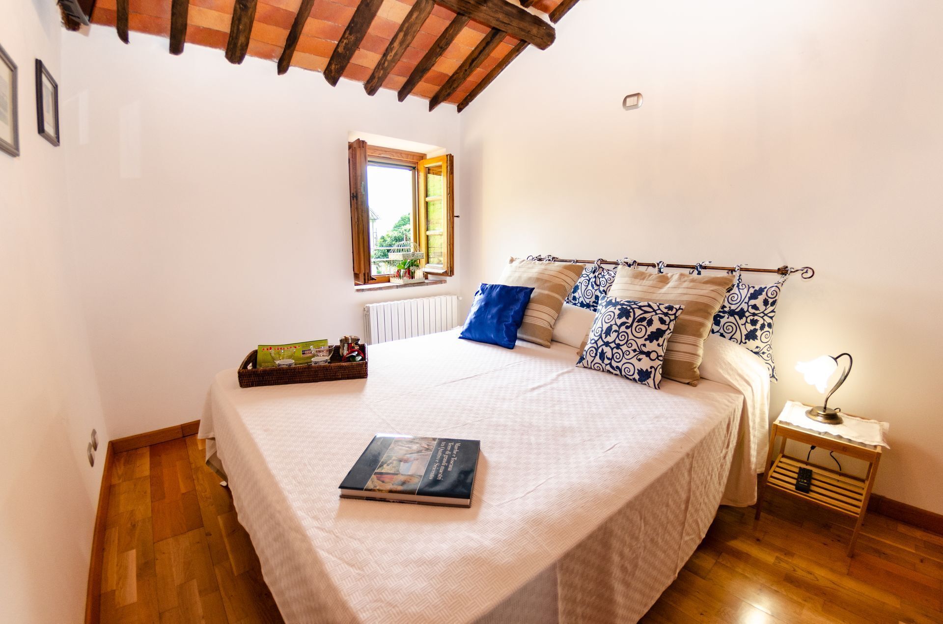 A bedroom with a large bed, a window, a bedside table with a lamp, and a wooden floor.