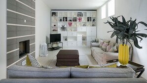 Ett modernt vardagsrum med en grå soffa, en tv, en bokhylla och en stor växt.