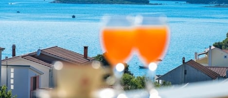A glass of orange juice in the foreground with a view of a coastal town and water in the background.