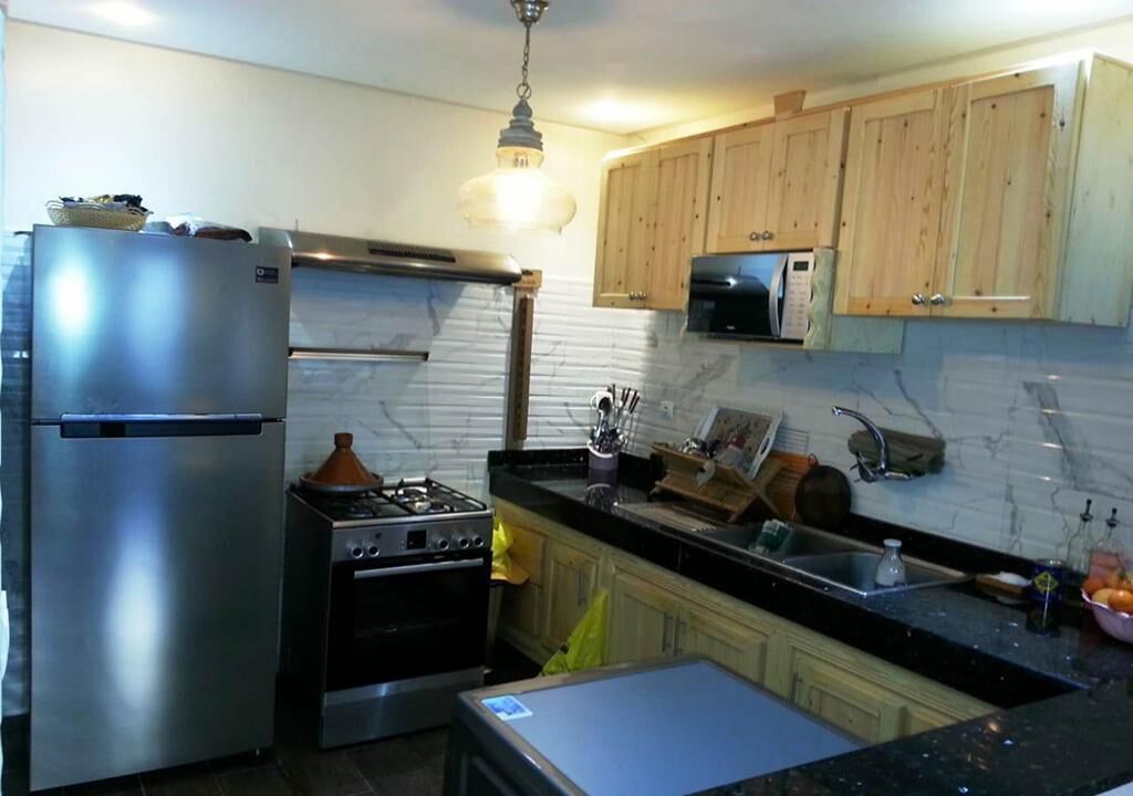Una cocina con refrigerador de acero inoxidable, estufa a gas, gabinetes de madera, microondas y un lavadero.