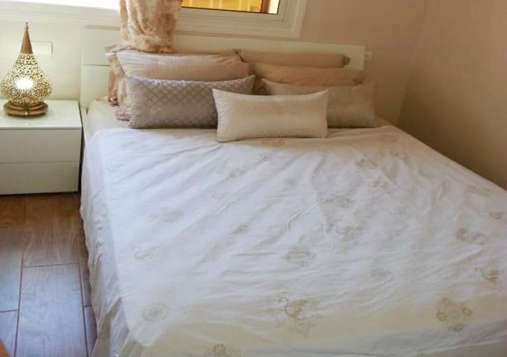A neatly made bed with a floral bedspread and multiple pillows, a bedside lamp, and a nightstand.