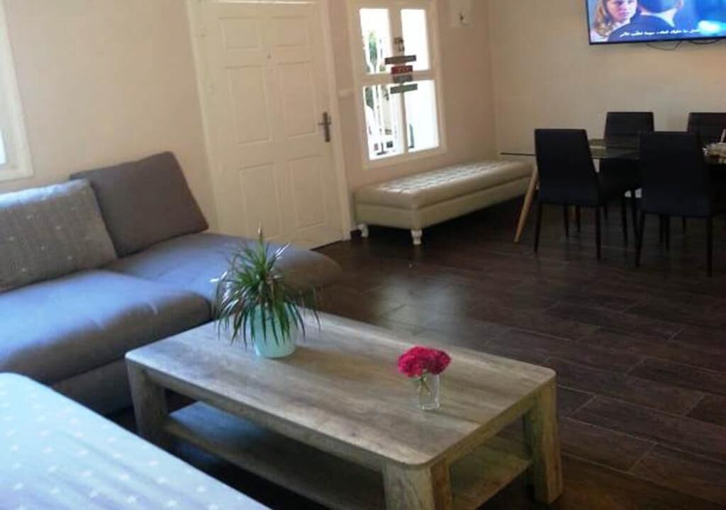 A living room with a sofa, a wooden coffee table with a vase of flowers, a bench, and a dining area with chairs and a table.
