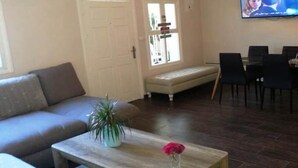 Een woonkamer met een bank, een houten salontafel met een bloevas, een zitbank en een eethoek met stoelen en een tafel.